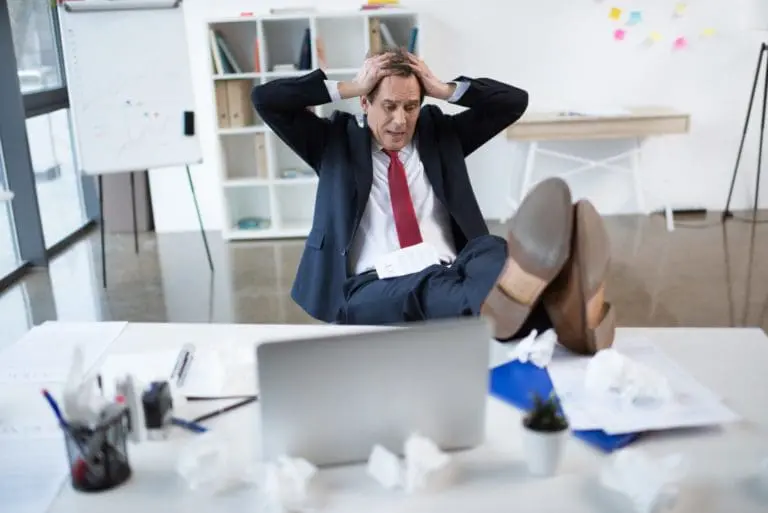 Stressed mature businessman sitting at table with laptop and gesturing