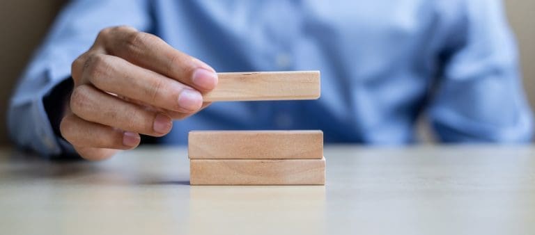 Businessman hand holding wooden building blocks on table background.