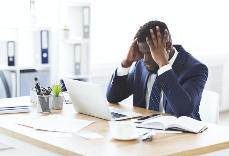 Stressed african businessman sitting in office with hand on forehead