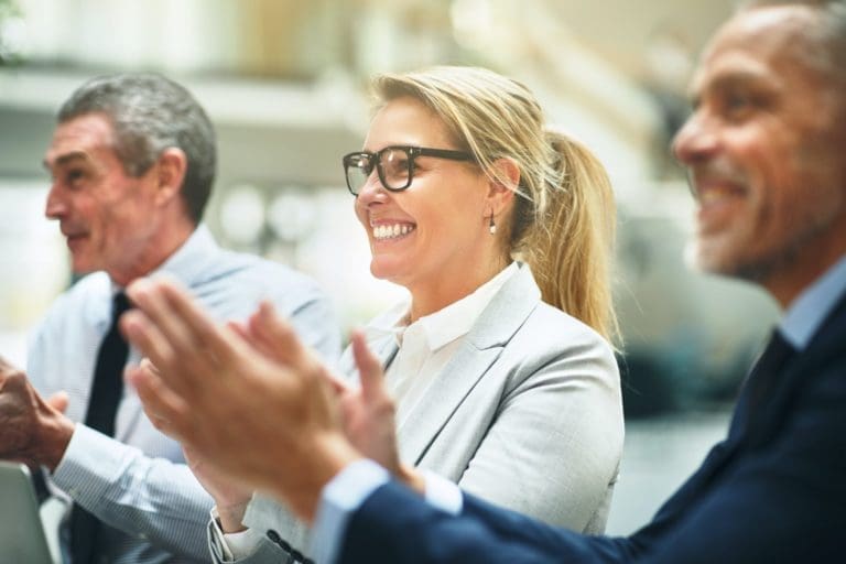 Three mature businesspeople smiling and clapping during an office seminar